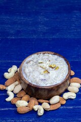 Closeup of Cracked Wheat Kheer or Payesh Garnished with Cashew, Pistachio, Almond in a Wooden Bowl Isolated on Blue Wooden Background with Copy Space, Also Known as Milk Pudding, Ksheeram