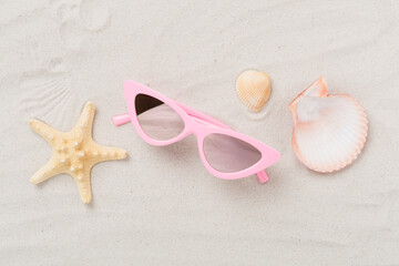 Stylish sunglasses on sand background, top view
