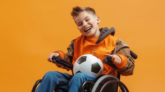 Happy little boy in wheelchair with football on yellow background. Sports for disabled people