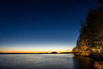 night landscape with starry sky on the shore of a lake in spring