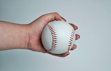 Hand with brown nail polish holding white and red baseball soft ball equipment sphere object photography isolated on horizontal ratio plain white or light gray background.