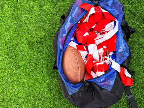 Flag Football Equipment on Green Turf. A large athletic duffel bag is filled with equipment for flag football play. Red and blue flags and a football fill the bag. Green turf football field background - Powered by Adobe