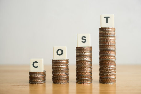 Word COST and stack coins as increase graph on wooden table with white wall background copy space. Cost of living and material industry increase in inflation crisis, merchandise price rise up concept.