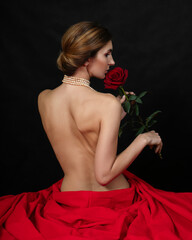 A naked girl is sitting in a red cloth and sniffing a rose