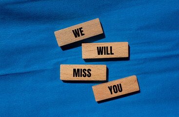 We will miss you words written on wooden blocks with blue background. Conceptual we will miss you...