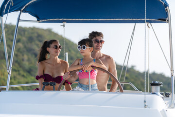 Mother and Father teaching their daughter how to drive speedboat or yacht, concept of family holiday vacations, togetherness and relaxation. Family luxury and carefree seascape or ocean explore trip.