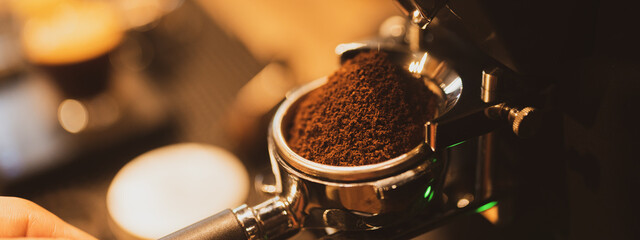 A professional barista. Concept of modern warm coffee shop and Preparing process of coffee. Close up of a hand holding a filter holder with ground coffee in a Cafe or coffee shop.
