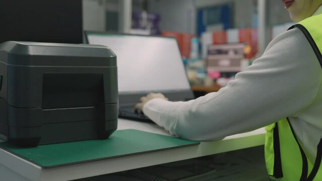 Woman uses a laptop or notebook to print bar code stickers on a bar code printer. Selective focus at sticker barcode.