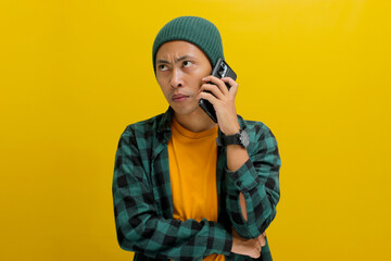 Annoyed Asian man, dressed in beanie hat and casual clothes, engages in a phone conversation,...