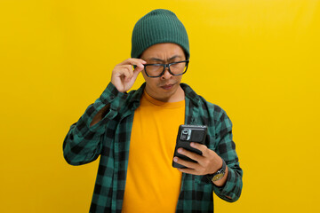 Asian man, dressed in a beanie hat and casual shirt, adjusts his eyeglasses while engrossed in...