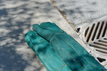 two loose bolts of green mesh netting discarded on a sidewalk by a storm drain cover