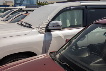 Fototapeta premium white car windshield is covered with white bedsheet to prevent heating on a parking lot at hot sunny summer day in Asia, closeup