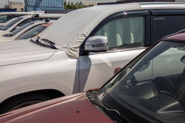 white car windshield is covered with white bedsheet to prevent heating on a parking lot at hot...