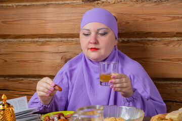 A Muslim woman in a lilac hijab at the table begins Iftar with inik and water the end of Ramadan