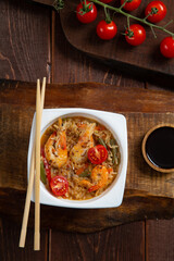 Rice with shrimp, yaki soba sauce on a wooden stand next to cherry tomatoes, soy sauce and chopsticks