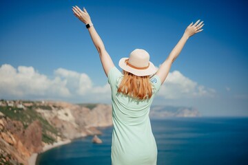 Woman tourist sky sea. Happy traveler woman in hat enjoys vacation raised her hands up