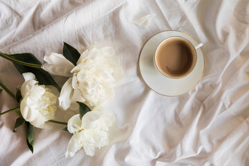 Morning coffee and peony flowers in bed. A tranquil morning routine with a cup of coffee amidst fresh white peonies on a soft linen textile background, conveying a sense of calm, serene, slow living. © magic_cinema