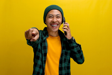 Confident Asian man, dressed in a beanie hat and casual shirt, pointing a finger at the camera,...