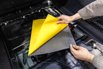 Auto service worker installing soundproofing foam material on car door trim from inside, tuning car...