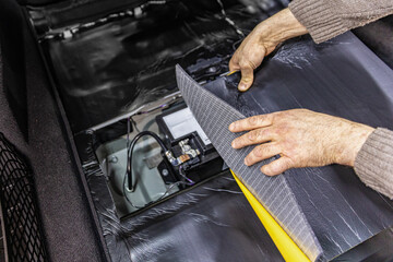 Auto service worker installing soundproofing foam material on car door trim from inside, tuning car...