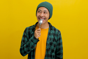 Curious Asian man in a beanie hat and casual shirt, holds a spoon near his mouth, envisioning...