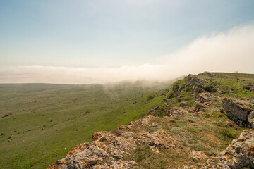 A foggy mountain top with a clear blue sky in the background. The sky is filled with clouds, giving the scene a serene and peaceful atmosphere.