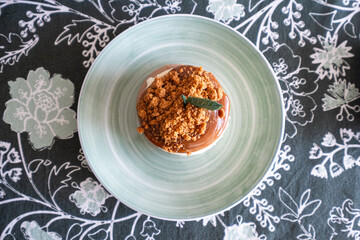 Top view. Detail of a A small round cheesecake on a plate on a beautiful tablecloth with floral decoration