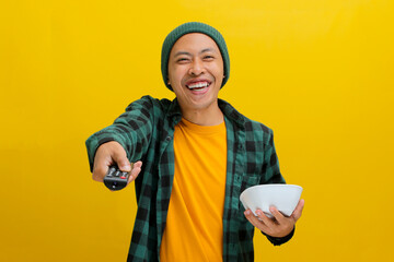 An enthusiastic young Asian man, dressed in a beanie hat and casual shirt, increases the TV volume...