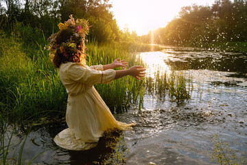 girl in flower wreath stand in river. summer nature background. Floral crown, symbol of summer...