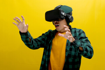 Excited Asian man wearing a VR headset reaches out with his hand, seemingly interacting with a...