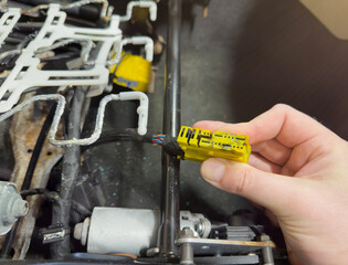 Repairing automotive electrical wiring. An auto electrician holds a connector of the car's electrical wiring in their hand, which has become covered with rust. Water ingress into the car's devices.