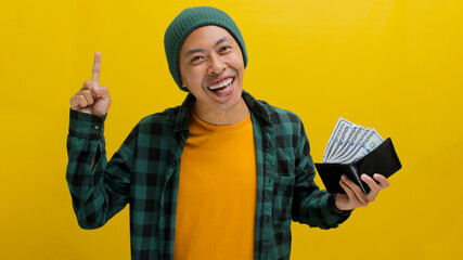 Excited young Asian man, dressed in a beanie hat and casual shirt, points his finger up, signifying...
