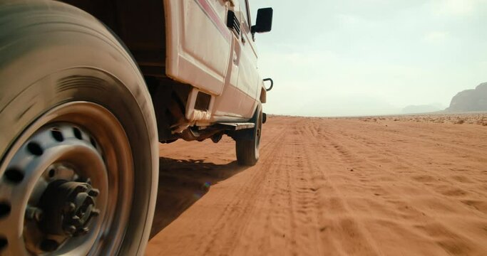 Closeup wheel of Off-road car tour in Wadi Rum Desert in Jordan. Adventures in Landmark Sand Valley of the Moon - tourist site in Middle East. 4K low angle view gimbal shot in slow motion