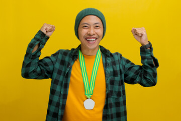 Happy young Asian man, dressed in a beanie hat and casual shirt, raises a clenched fist in...