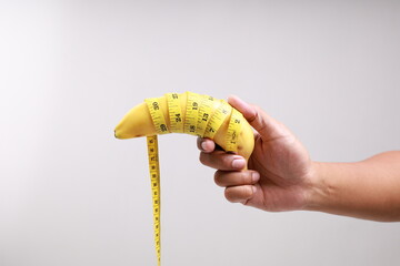 Man's hand holding a yellow banana with measure tape. Men's health concept.
