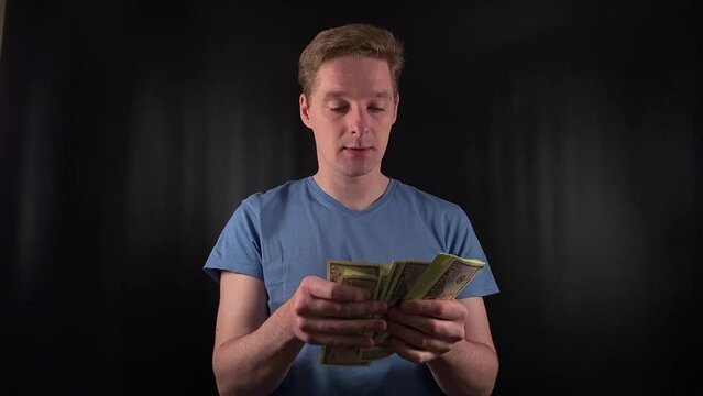 a dashing young man enthusiastically counts a stack of dollar bills. The thrill of a life-changing stroke of luck on the simple black backdrop. The epitome of celebratory joy after hitting the jackpot
