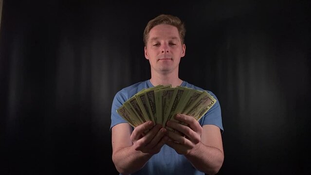 a dashing young man enthusiastically counts a stack of dollar bills. The thrill of a life-changing stroke of luck on the simple black backdrop. The epitome of celebratory joy after hitting the jackpot