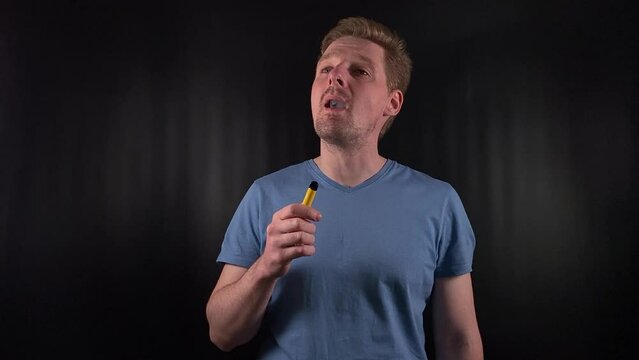 a stylish young man exhales a thick cloud of vapor, e-cigarette. With a casual, unbothered expression set on the stark black backdrop, youthful indulgence and the cavalier embrace of trending habit