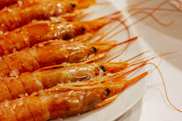 Fresh orange boiled king shrimps on a white plate on a table. Whole cooked delicious seafood served in restaurant. Large prawns with long mustache.