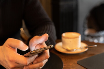 Men's hands on the table use mobile phone in a café or restaurant. A male hands holding smartphone. Work, technology, communication. Real person