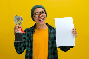 Cheerful Asian student wearing eyeglasses and a casual shirt, holding a piece of paper and a...