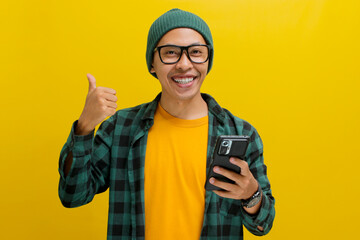 Smart young Asian man, sporting eyeglasses and dressed in a beanie hat and casual shirt, gives a...