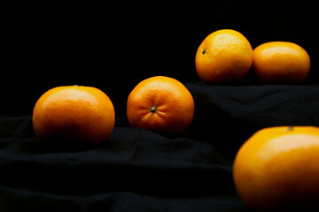 Orange fruits with a black background. Beautiful still-life orange with a dark theme. Ripe oranges are placed on a black fabric, an organic and fresh fruit that is good for health. Black background.