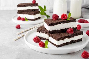 Chocolate cake with milk cream filling on a white plate with fresh raspberries and mint with bottles of milk. Delicious dessert. Copy space.
