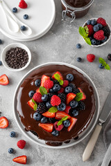 Delicious chocolate cake with chocolate glaze and fresh berries on a white plate on a gray concrete background.