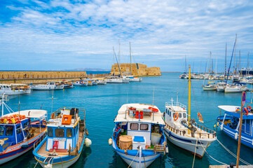Colorful boats in the old venetian port of Herakleio in Crete, Greece. The koule fortress in the background