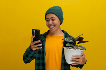 Cheerful Asian man in a beanie and casual clothes smiles while checking his phone, holding a...