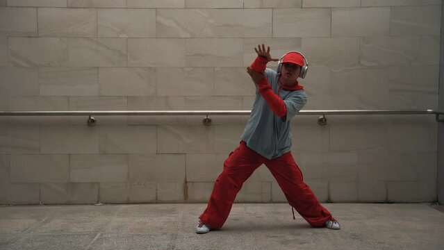 Handsome choreographer practice street dance in gray background. Young attractive b boy dancer perform while wearing stylish cloth. Feeling of lively step. Copy space. Outdoor sport 2024. Sprightly.