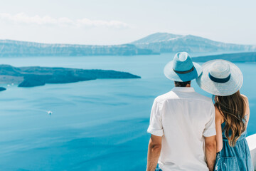 Fototapeta premium Young couple in hats enjoy sea views from a rooftop terrace on a Greek island. Rear view. Concept of honeymoon, vacation and summertime travel.