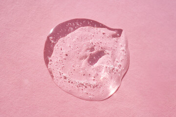 Drop of serum shimmering in the sun on a pink background.